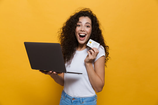 Photo of shopping woman 20s wearing casual clothes holding black laptop and credit card, isolated over yellow background