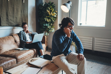 Workplace situation. Two people in the office together. Man talking on mobile phone and woman working with laptop