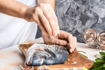 Process of cooking Dorado fish with lemon, olive oil and herbs. Female hands close-up. Concept of homemade food, culinary hobby