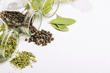 Popular spices in small jars scattered on white background. Sea salt, bay leaf, pepper and herbs.