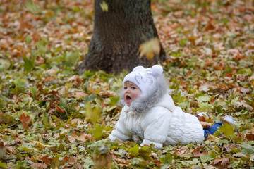 Little girl, with emotional expression of her face, lies on dry orange fallen leaves in autumn parkland