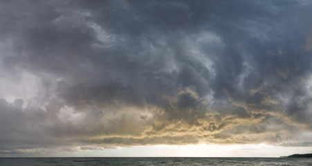 Beautiful lead clouds in front of a storm at sea at sunset. Panorama
