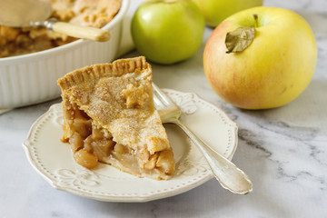 A traditional American apple pie decorated with stars and sugar, apples and cinnamon on a light background.