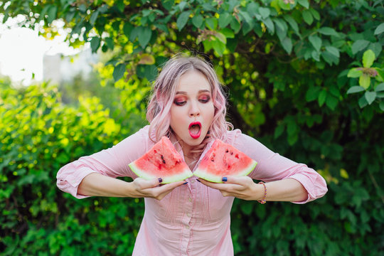 Beautiful young woman with pink hair holding two slices of watermelon