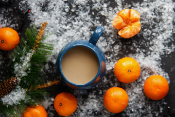 Fototapeta na wymiar Christmas and New Year's concept. Mandarins, coffee mug, snow, Christmas tree branch. Against a dark background