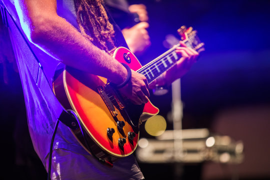 Guitarist playing on electric bass guitar on stage. Colorful, soft focus and blur background