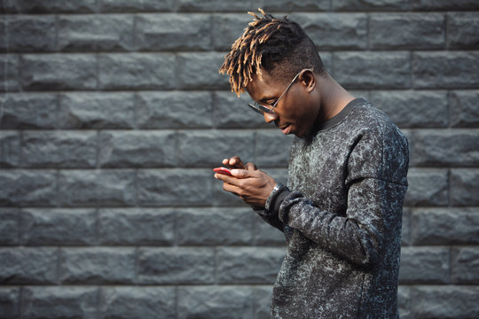 African american man using mobile phone app at brick wall background - Powered by Adobe