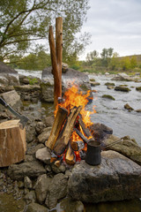 Aromatic and hot coffee on the fire. Bonfire and thermo mugs. Bonfire on the river bank.