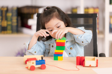 Lovely cute little Asian girl in jeans shirt playing wood block toys on desk. Concept for funny...