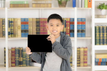 Young Asian boy smiling and hold digital tablet blank screen in library. Educational Ideas And learning for the future