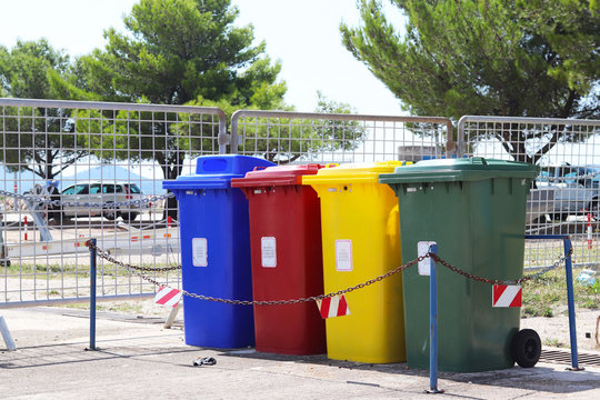 Four multicolored boxes for sorted garbage: red, green, blue and yellow. Recycling garbage in the tourist area. Infrastructure of the Mediterranean marina. Plastic waste containers.