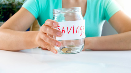 Closeup image of young woman holding glass jar with few coins in it