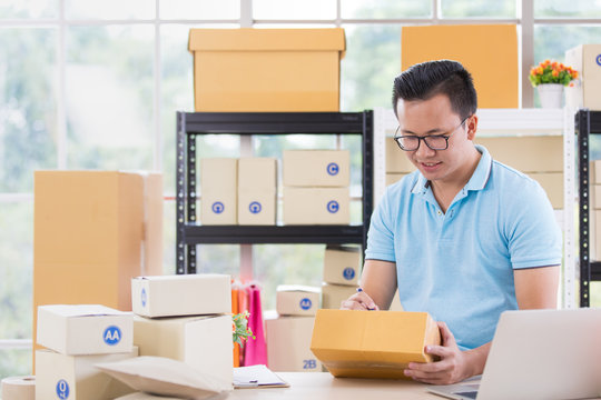 Young Asian businessman in casual shirt write on parcels,  working in simple house office look like doing startup business. Concept for online marketing, SME and home base workplace