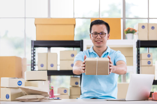 Asian businessman in casual shirt hold in parcels on hand,  working in simple house office look like doing startup business. Concept for online marketing, SME and home base workplace