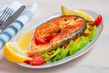 Roasted salmon steak on a plate with avocado and lemon close-up