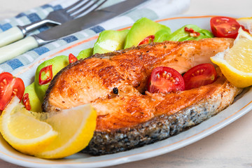 Roasted salmon steak on a plate with avocado and lemon close-up