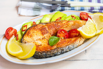 Roasted salmon steak on a plate with avocado and lemon close-up