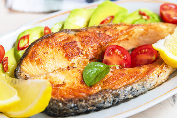 Roasted salmon steak on a plate with avocado and lemon close-up