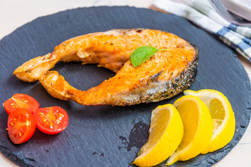 Roasted salmon steaks on the black slate plate with avocado and lemon close up