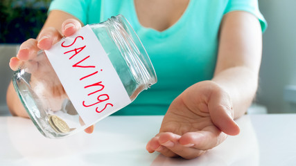 Closeup photo of young woman having financial problems emptying glass jar with money savings