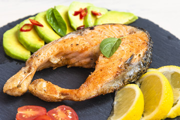 Roasted salmon steaks on the black slate plate with avocado and lemon close up