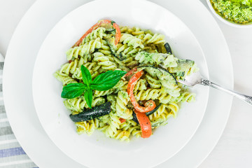 Italian vegetarian food - fusilli pasta with zucchini and pepper and pesto sauce on a white plate close-up, top view