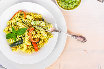Italian vegetarian food - fusilli pasta with zucchini and pepper and pesto sauce on a white plate close-up, top view, copy space