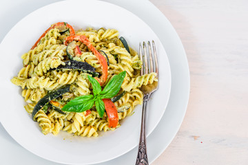 Italian vegetarian food - fusilli pasta with zucchini and pepper and pesto sauce on a white plate close-up, top view, copy space