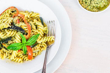 Italian vegetarian food - fusilli pasta with zucchini and pepper and pesto sauce on a white plate close-up, top view, copy space