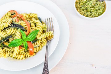 Italian vegetarian food - fusilli pasta with zucchini and pepper and pesto sauce on a white plate close-up, top view, copy space