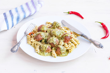 Italian traditional food - fusilli pasta with meatballs and pesto sauce on a white plate