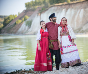 A man and two women in Russian national costumes pose for the camera on the background of an amazing landscape