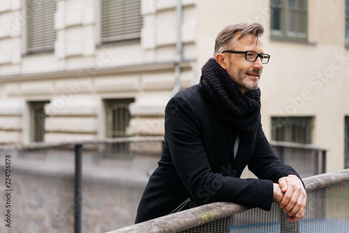 Man leaning on a bridge railing deep in thought