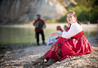 A girl in Russian national costume sitting on a sand on the background of an amazing landscape