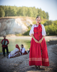 A beautiful girl in red Russian national costume stand on the background of an amazing landscape