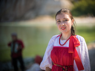 A girl in red Russian national costume stand on the background of an amazing landscape close up shot