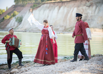 Beautiful young people in Russian national costumes dancing, playing accordion