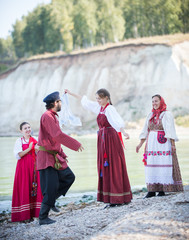 Young people in Russian national costumes dancing folk dances on the background of an amazing landscape