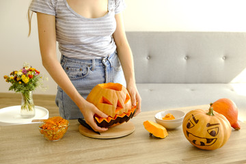 Close up of young woman carving Jack O Lattern from ripe orange pumpkin with knife on her wooden...