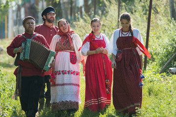 Group of men and women in russian folk costumes in nature. The man plays the accordion. Celebration