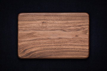 Handmade black walnut rectangular rounded wooden chopping board on black cotton, walnut texture background