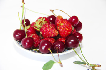   red berries of strawberries and burgundy cherries with green leaves on a plate isolated on white background