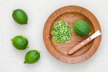 Several limes on burlap and some cut down lemon peel on teak plate
