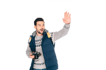smiling young man with backpack holding camera and waving hand isolated on white