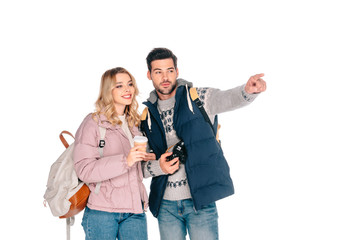 young couple of tourists with backpacks holding coffee to go and camera while pointing and looking away isolated on white