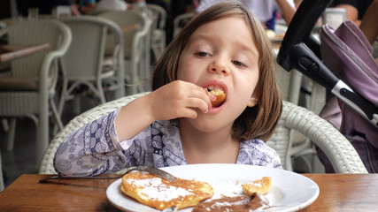 A child reluctantly eats pancakes with chocolate.