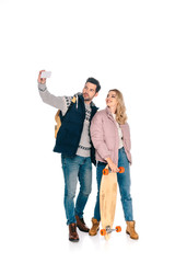 smiling young couple with backpack and skateboard taking selfie with smartphone isolated on white