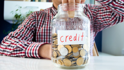 Closeup photo of young man putting coins in glass jar