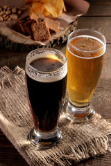 A glass of light and a glass of dark beer and snacks in the background on a wooden brown table