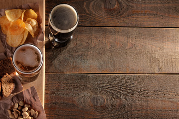 A glass of light and a glass of dark beer and snacks on a wooden brown table with a place for inscription. view from above